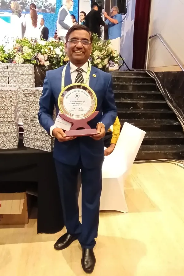 Dr. Ramakant Patil in a blue suit, smiling and holding a circular plaque at a conference venue.