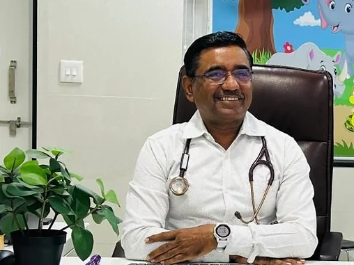 Dr. Ramakant Patil in a white shirt with a stethoscope, smiling at his desk, a children’s jungle mural on the wall behind him.
